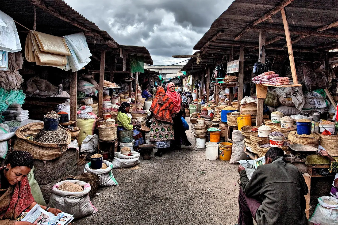 Stalls piled with grain, beans and baskets along a covered aisle of the central market in Arusha